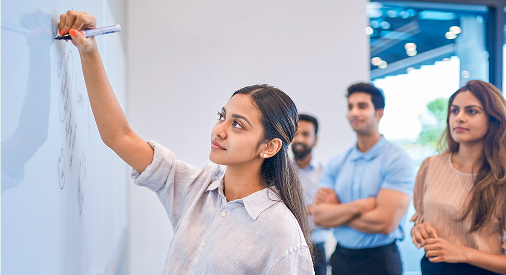 Student writing on a whiteboard with other students